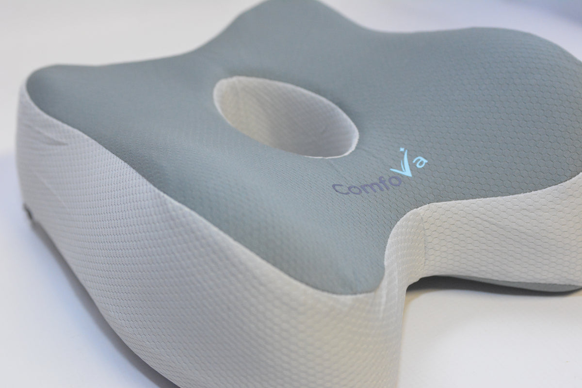 A close-up of a contoured neck pillow with a light gray top and off-white textured sides, featuring the brand name 'ComfoVia' embroidered on the side.