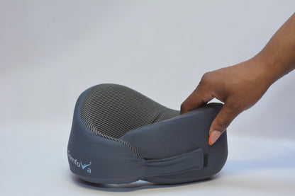 A dark gray contoured neck pillow with a textured striped interior, shown with a hand pressing down on the side to demonstrate its soft, flexible support.