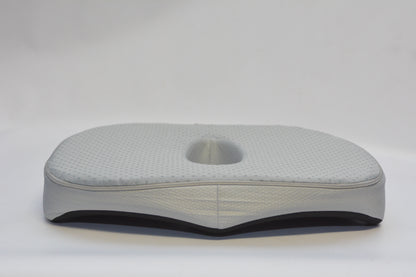 A light gray contoured lumbar support pillow with a central cutout, featuring a textured top surface and a black base, photographed on a seamless light gray background.